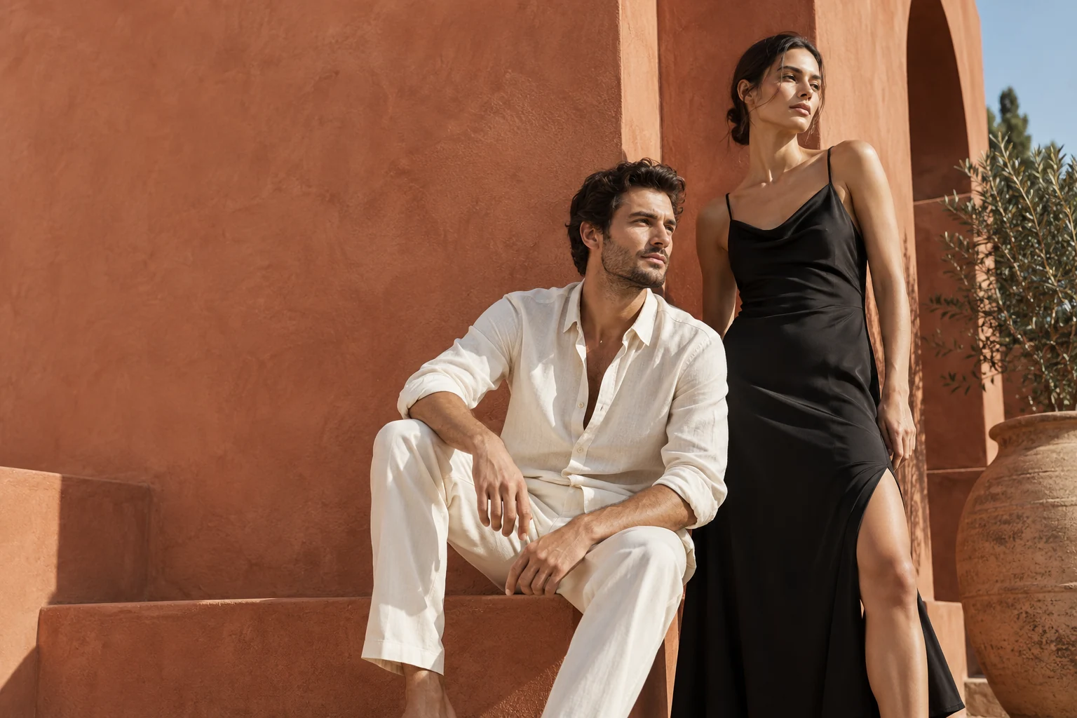 Deux mannequins adultes portant une tenue ivoire et une robe noire devant une architecture terracotta